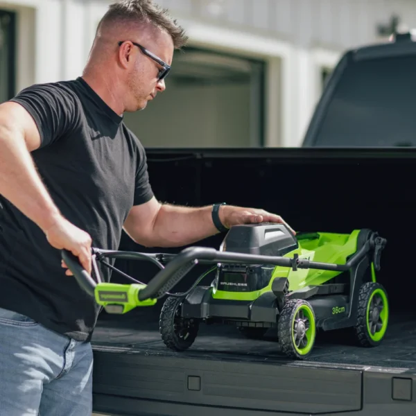 Greenworks 36 cm sláttuvél með samanbrotnu handfangi lyft upp á pall bifreiðar.